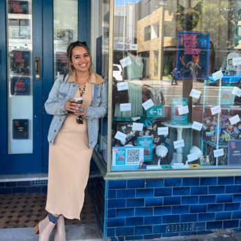 Woman holding a coffee and smiling outside a shop with blue tiles and window displays.